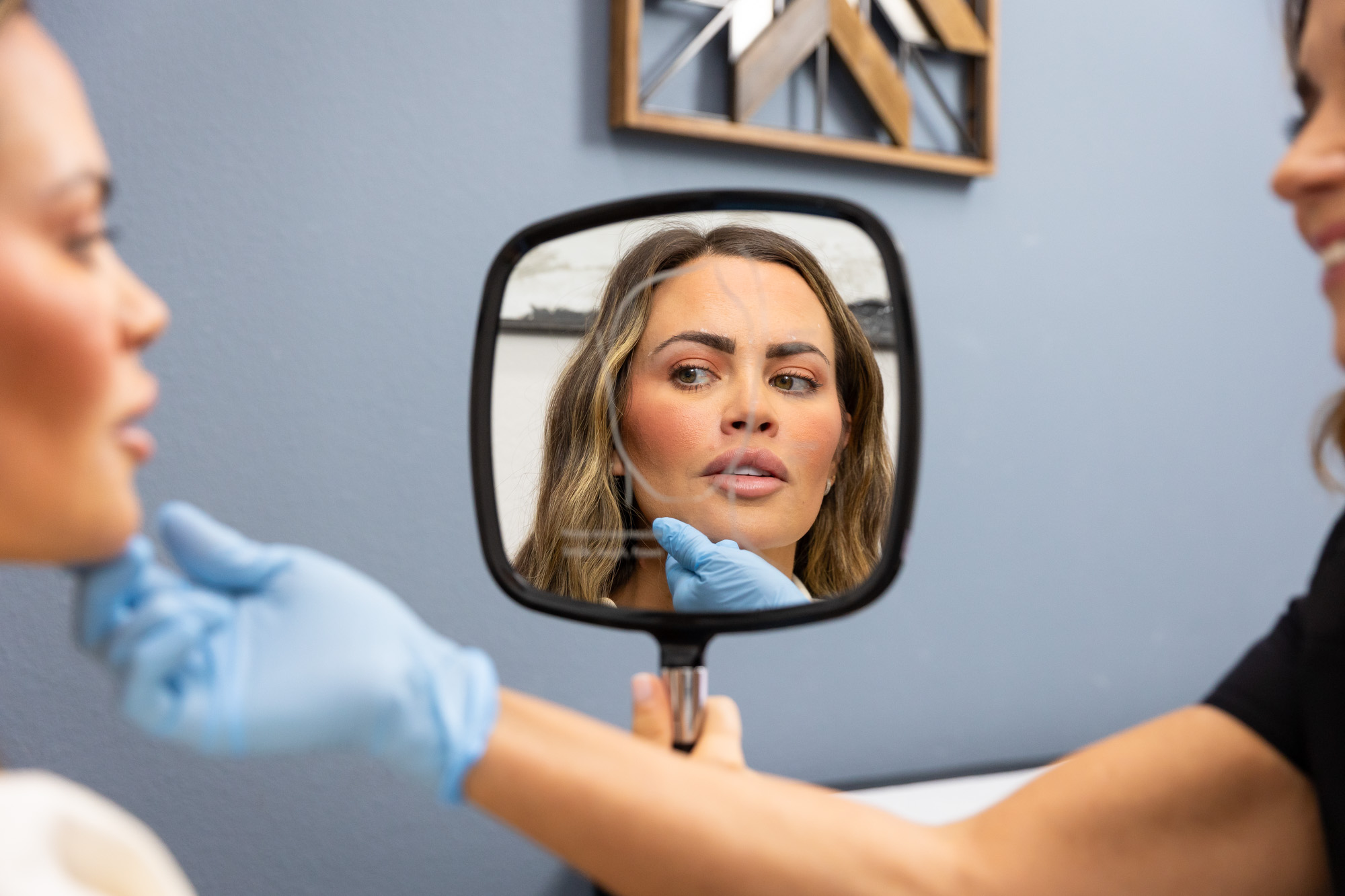A patient at The Institute for Hormonal Balance looks in a handheld mirror as a provider assesses her skin before facials near Mansfield.