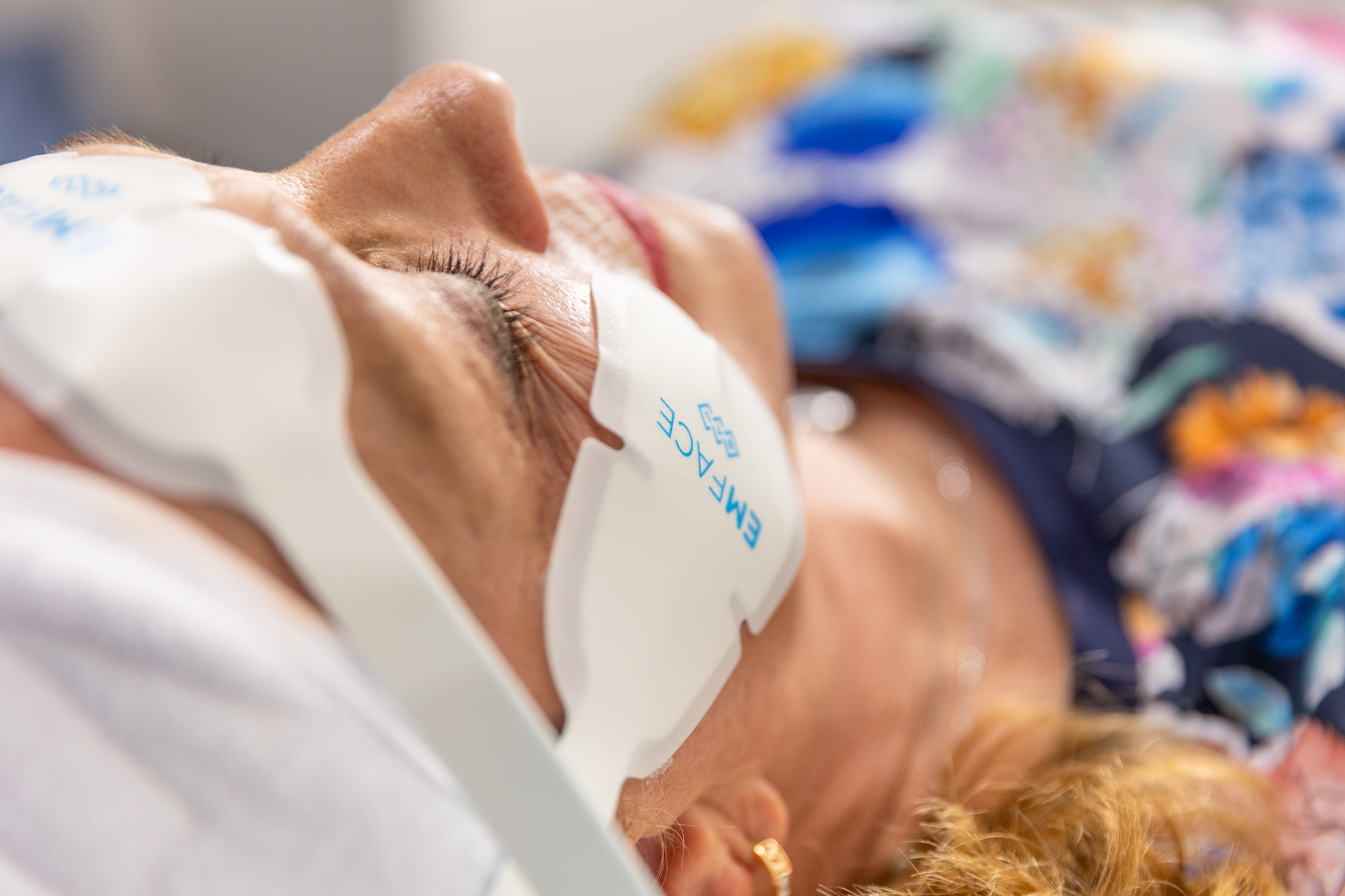 A patient is lying on her back as she receives an Emface treatment to compliment her recent lip fillers in Arlington. The special Emface applicators rest on her cheeks and forehead, working to give her skin a natural boost for a full face refresh alongside her filler.