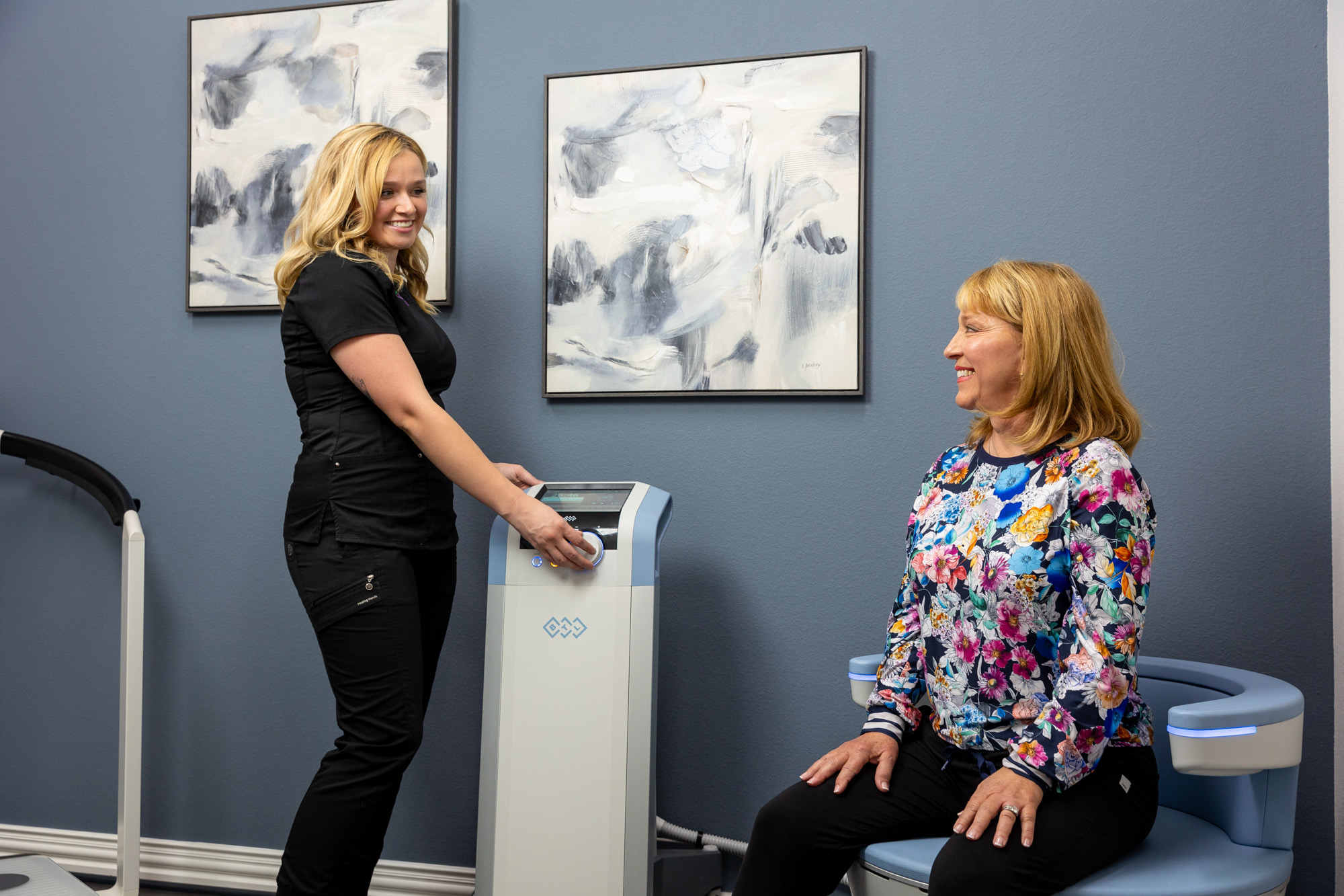 A provider stands next to the Emsella device as a mature female patient sits on the Emsella chair. This therapy provides pelvic floor therapy as part of a treatment plan for gynecology near Fort Worth.