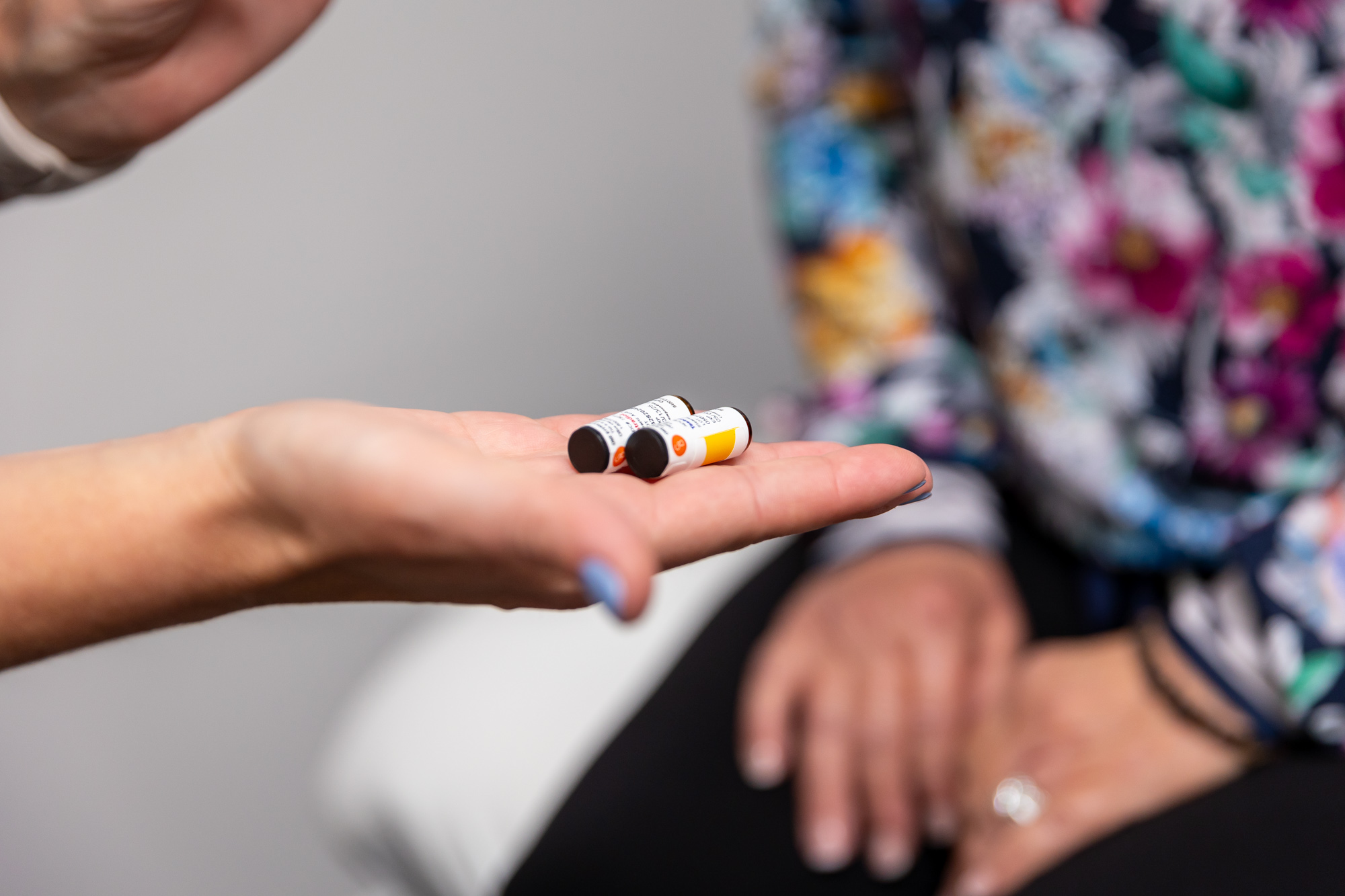 A provider's hand is held palm-up, showing 2 containers or hormone replace therapy pellets to a patient as part of their urinary incontinence treatment in Arlington.